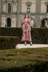 Modelo luciendo el Carina Dress en estampado Tucanes Palmeras, vestido midi envolvente con mangas globo en un jardín.